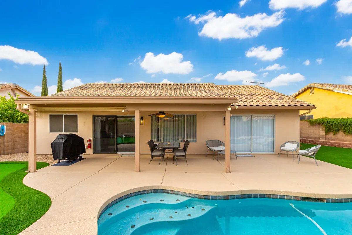 An inviting outdoor scene with a private pool, patio seating area, and a grill. The area is bathed in natural light, suggesting a perfect setting for swimming, barbecuing, and dining al fresco with family and friends.