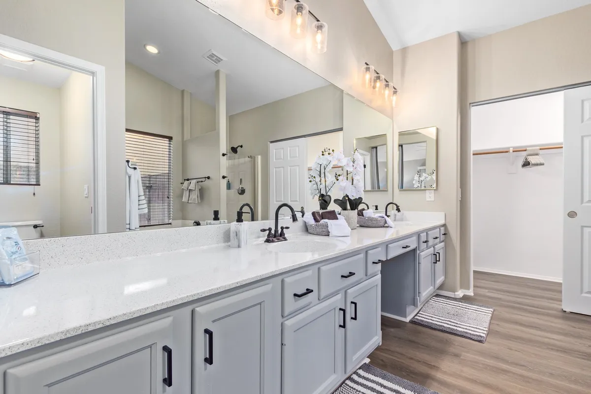 A sophisticated ensuite bathroom with a double vanity, expansive mirrors, decorative orchids, and modern light fixtures. The clean, spacious design creates a true spa-like ambiance ideal for relaxation and morning routines.
