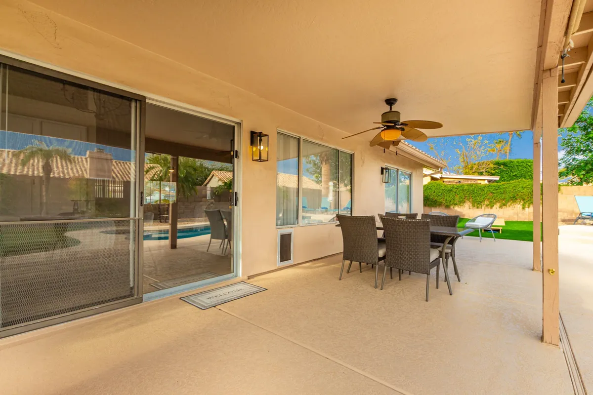 This scene highlights an outdoor dining area with a table set under a ceiling fan, overlooking a swimming pool in the background. The space beckons guests for al fresco meals or relaxing beside the pool.