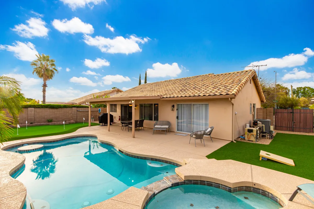 The photograph showcases a beautifully landscaped yard with a shimmering swimming pool, comfortable patio furniture, and swaying palm trees. The atmosphere is relaxed and cheerful, perfect for gatherings or unwinding after a day outdoors.
