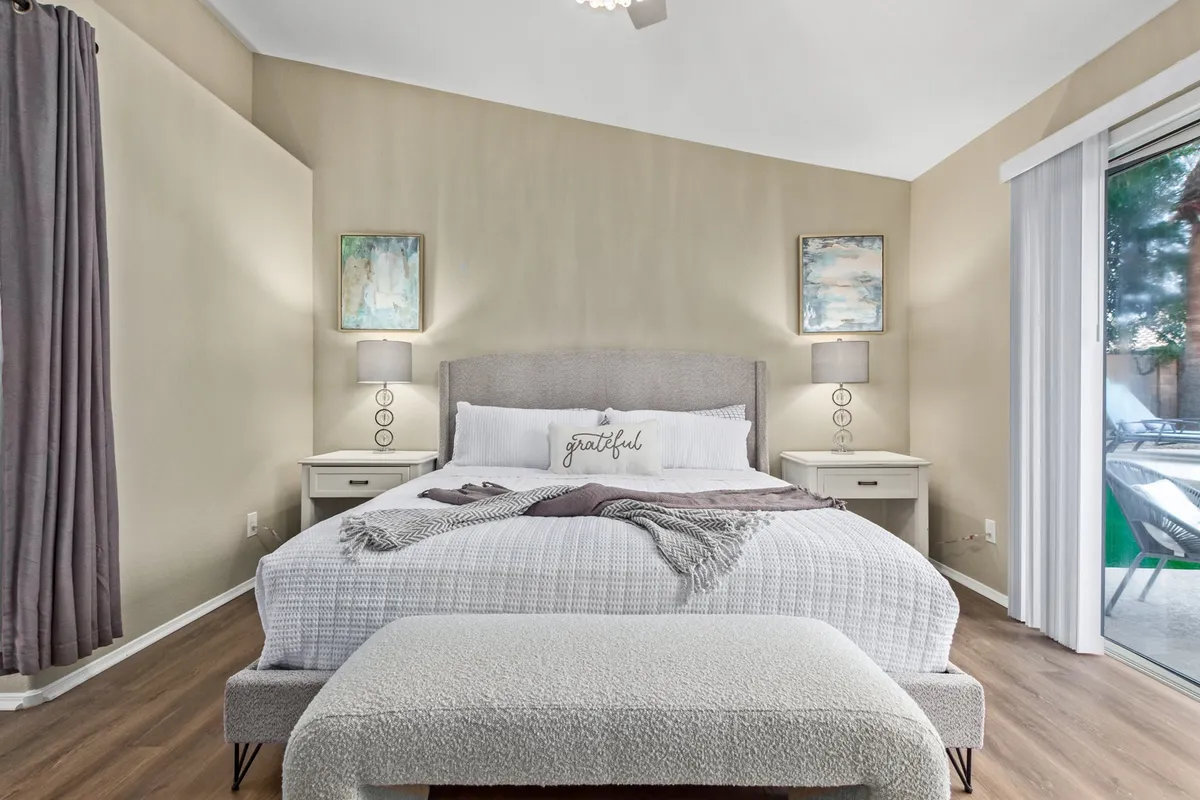 A peaceful additional bedroom with a comfortable bed, decorative pillows, nightstands, artwork, and a sliding glass door allowing plenty of natural light to flood the space. The room exudes calm and privacy.