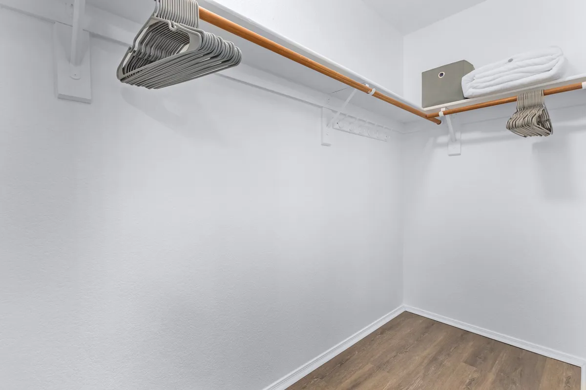 A well-organized walk-in closet featuring a wooden clothing rod, hangers, and neatly stacked shelves with towels and a storage box. The minimalist design ensures ample space for planning outfits and storing belongings.
