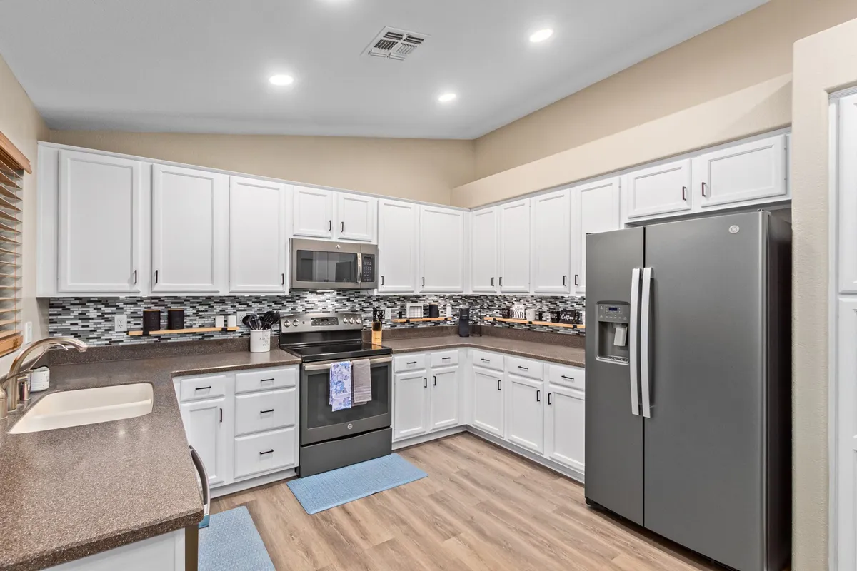 A bright kitchen featuring white cabinetry, stainless steel appliances, a textured mosaic backsplash, and a spacious solid surface countertop. The room exudes warmth and is clearly designed for both daily meals and special gatherings.